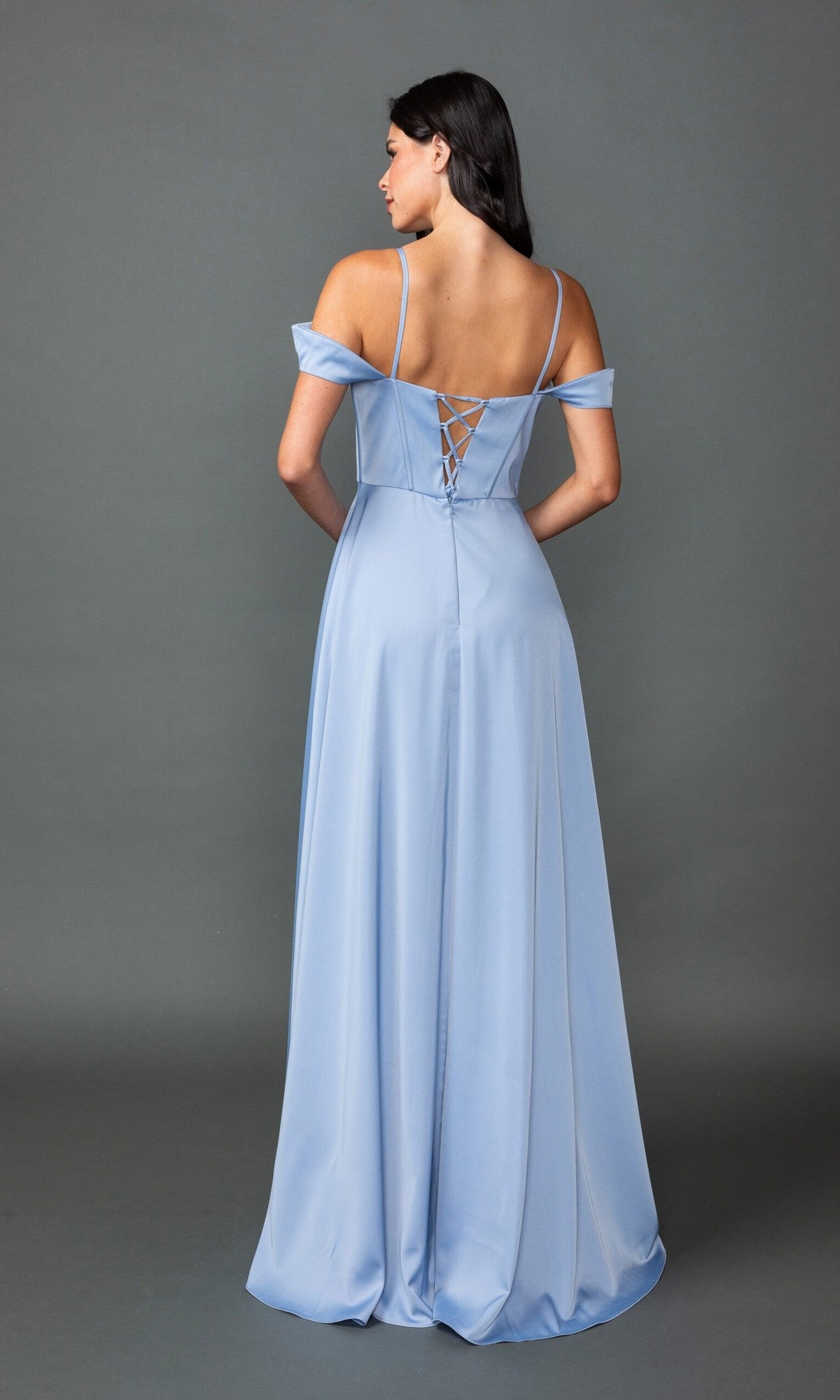 A woman stands facing away from the camera against a gray background, wearing the Dancing Queen 4544 long prom dress—a light blue, floor-length A-line gown with off-the-shoulder sleeves and a lace-up back.